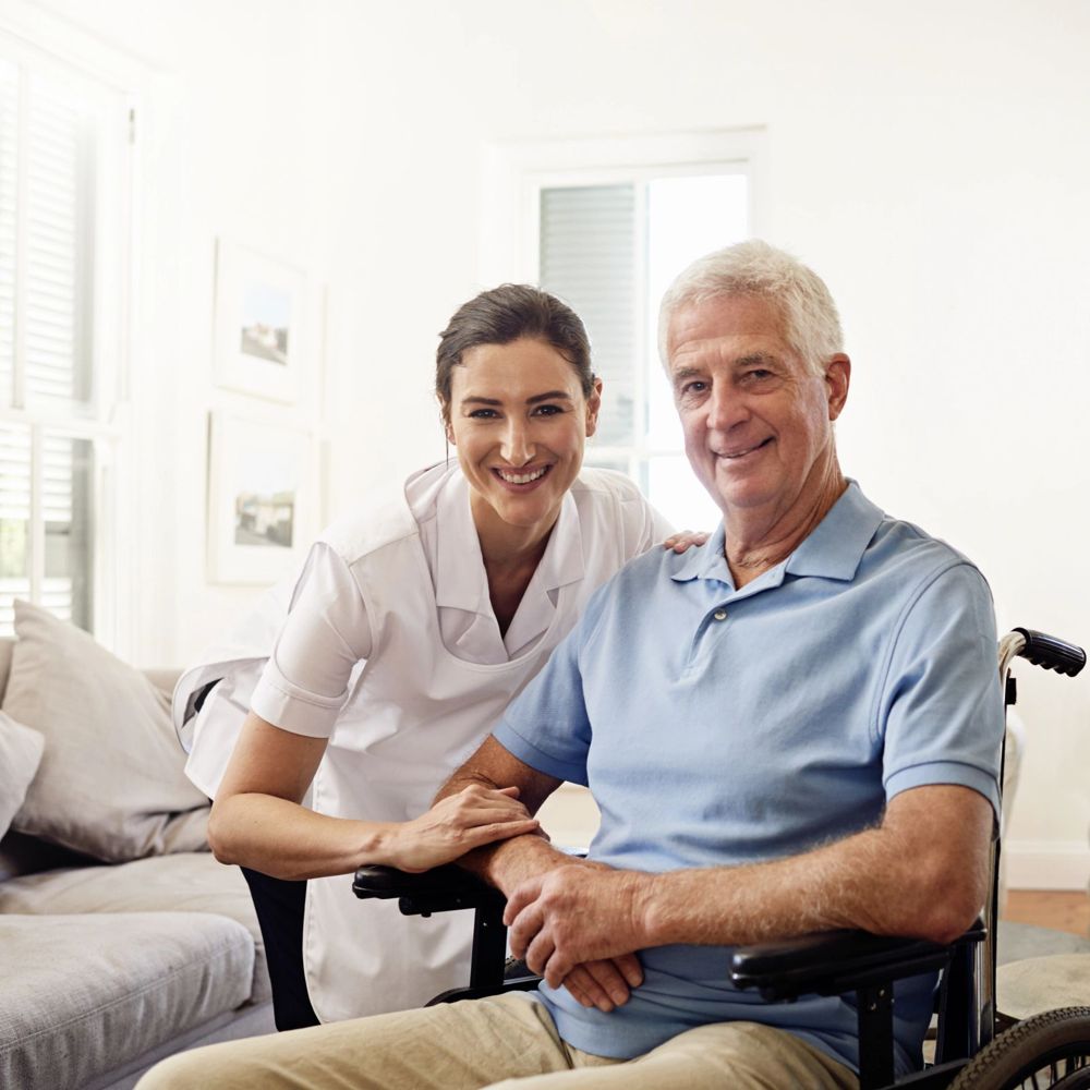 A caregiver sitting beside a smiling senior man in a bright living room